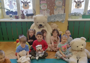Dzieci siedzą na dywanie i trzymają pluszowe niedźwiadki.