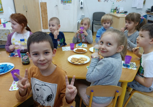 Dzieci siedzą przy stoliku i pozują do zdjęcia.