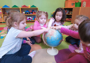 Dzieci wskazują palcem na globusie miejsce, gdzie żyją niedźwiedzie polarne.