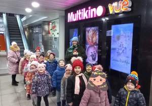 Dzieci stoją i pozują do zdjęcia przed kinem.