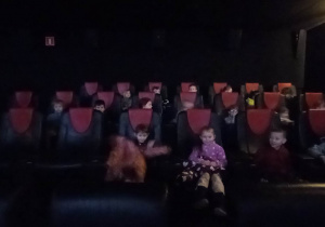 Dzieci siedzą na fotelach w sali kinowej.