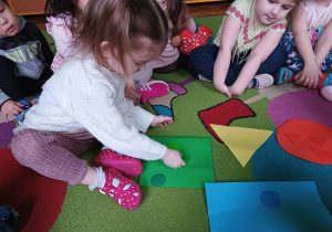 Dzieci siedzą na dywanie i dopasowują figury według koloru.