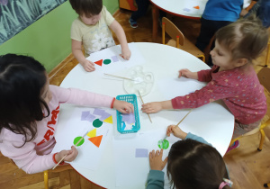 Dzieci siedzą przy stoliku i wykonują pracę plastyczną.