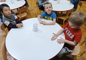 Chłopcy siedzą przy stoliku i trzymają w dłoniach fasolki.