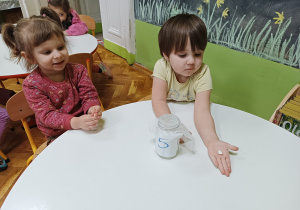 Dziewczynki siedzą przy stoliku i trzymają w dłoniach fasolki.