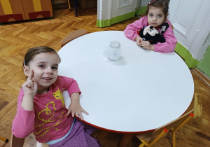 Dziewczynki siedzą przy stoliku i pozują do zdjęcia.