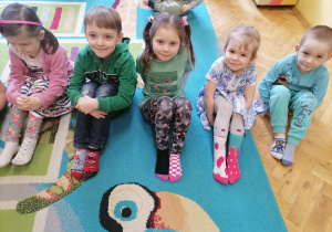 Dzieci siedzą na dywanie i pokazują dwie inne skarpetki.