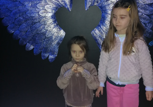 Dziewczynki stoją przy świetlistych skrzydłach.