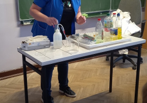Pani Ewa pokazuje eksperyment z wodą przy stole.