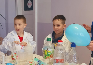 Dzieci stoją przy stole i wykonują eksperyment z balonem.