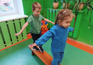 Dzieci przechodzą po ławeczce z wyprostowanymi rękoma.