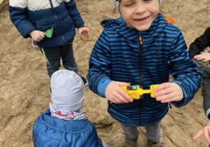 Uśmiechnięty chłopiec stoi i pozuje do zdjęcia w piaskownicy.