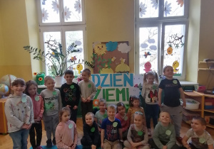 Dzieci stoją i siedzą przy tablicy z napisem Dzień Ziemi.