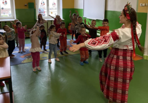 Dzieci naśladują ruchy za instruktorką w ukraińskim stroju ludowym.