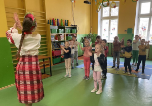 Dzieci naśladują ruchy za instruktorką w ukraińskim stroju ludowym.