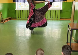 Dzieci siedzą i oglądają pokaz taneczny instruktorki w ukraińskim stroju ludowym.