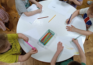 Dzieci siedzą przy stoliku i rysują wymarzony las.