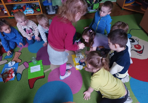Dzieci siedzą na dywanie i dopasowują odpady do danego pojemnika.