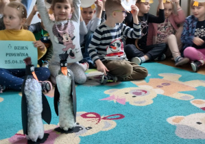 Dzieci siedzą i pozują do zdjęcia z wykonanymi pracami plastycznymi "Pingwin".