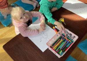 Dzieci siedzą i kolorują narysowane postacie.
