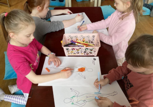 Dzieci siedzą i kolorują narysowane postacie.