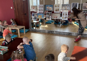 Dzieci siedzą przy stolikach i oglądają obrazy strojów aktorów.