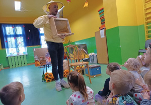 Zdjęcie Pana w stroju ochronnym pszczelarskim pokazującego pszczoły.