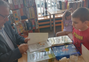 Mężczyzna wpisuje dedykację do książki dla chłopca.