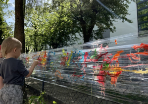 Chłopiec stoi i maluje pędzlem na folii.