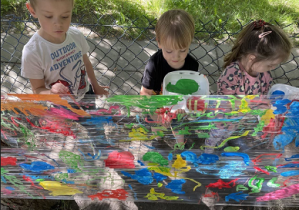 Zdjęcie dzieci stojących i malujących farbami na folii.