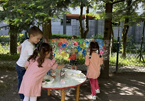 Zdjęcie dzieci stojących przy stoliku, na którym znajdują się farby i pojemniki z wodą.