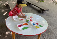 Zdjęcie chłopca stojącego przy stoliku z farbami i wodą.