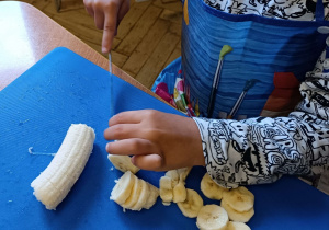 Zdjęcie chłopca krojącego banana na desce do krojenia.