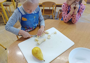 Zdjęcie dziewczynki krojącej banana na desce do krojenia.