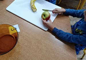Zdjęcie chłopców przy stoliku z owocami na desce do krojenia.