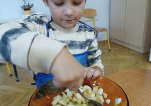 Chłopiec siedzi przy stoliku i miesza owoce w misce.