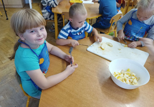 Dzieci siedzą przy stoliku i kroją owoce na sałatkę.