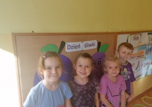Dzieci ubrane na fioletowo stoją przy tablicy.