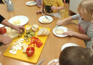 Dzieci stoją przy stole i smarują kromki chleba masłem.