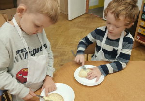 Chłopcy siedzą przy stole i smarują kromki chleba masłem.