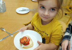 Zdjęcie dziewczynki trzymającej talerz z przygotowaną kanapką.