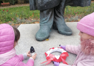 Dziewczynki kładą znicz i wianek na cokole pomnika.