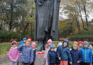 Dzieci stoją przed pomnikiem St. Staszica.