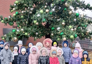 Dzieci stoją przed kolorowym drzewem.