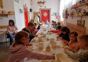Dzieci siedzą przy stole i lukrują zajączki.