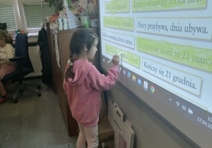 Dziewczynka stoi przy tablicy interaktywnej.