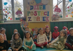 Dzieci siedzą na dywanie przy tablicy.