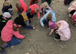 Dzieci piszą litery patykami po ziemi.