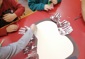 Dzieci przyklejają wycięte odciski dłoni.