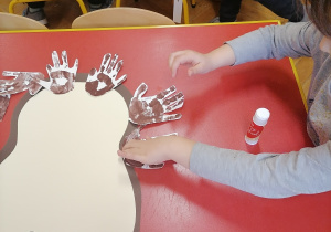 Dzieci przyklejają wycięte odciski dłoni.